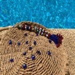 This unique bohemian-inspired Round Rattan bag crafted from natural fiber is adorned with small blue glass beads and a unique antique Afghan charm.